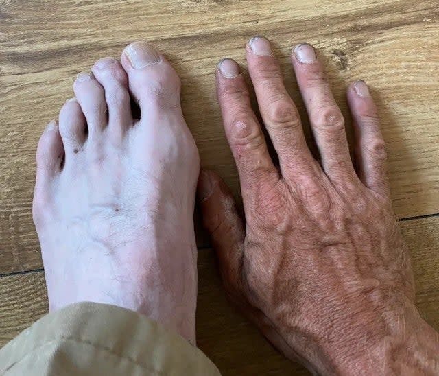 A very pale foot and a very suntanned hand that has lots of wrinkles