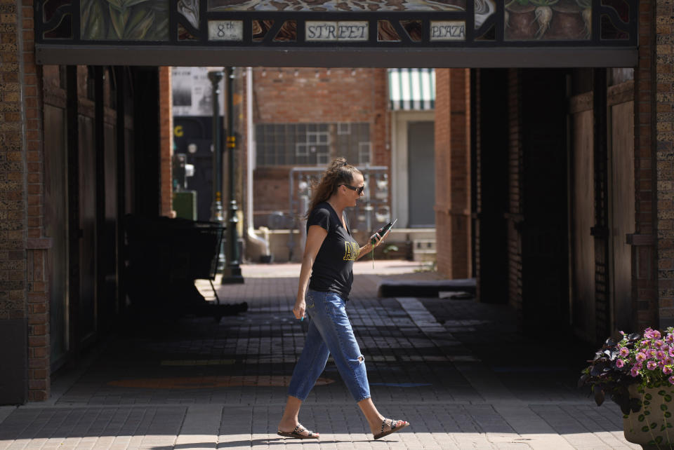 In this Friday, July 223, 2021, photograph, a pedestrian looks at a mobile device while walking down a downtown sidewalk in Greeley, Colo. Figures released this month show that population growth continues unabated in the South and West, even as temperatures rise and droughts become more common. That in turn has set off a scramble of growing intensity in places like Greeley to find water for the current population, let alone those expected to arrive in coming years. (AP Photo/David Zalubowski)