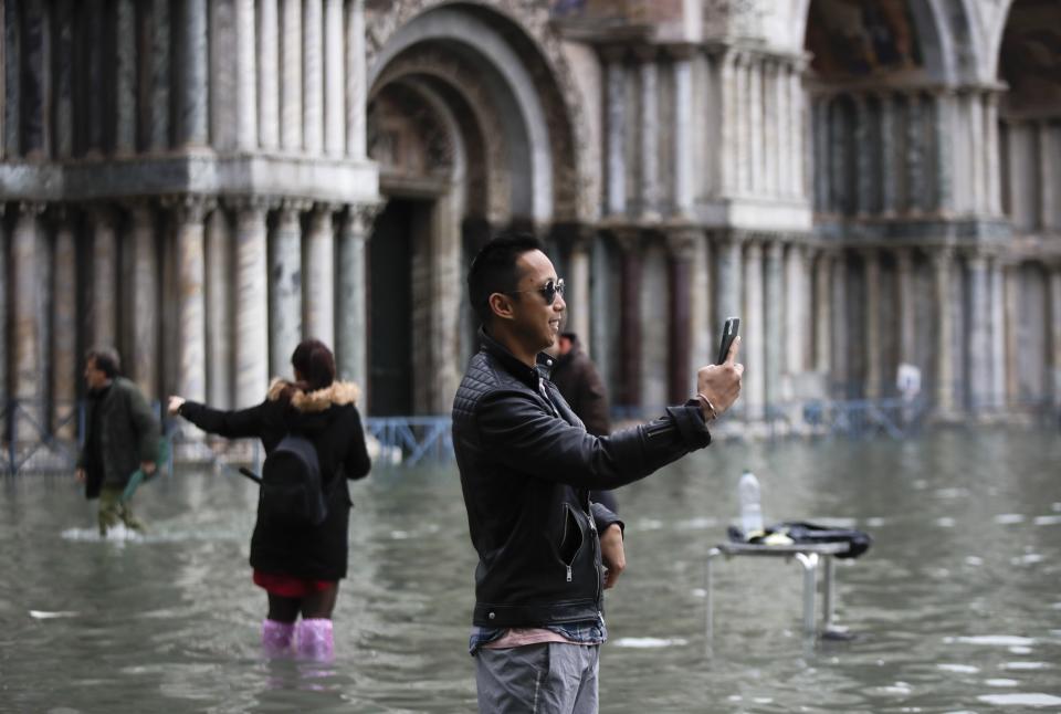 Tourists take pictures in a flooded St. Mark's Square, in Venice, Wednesday, Nov. 13, 2019. The high-water mark hit 187 centimeters (74 inches) late Tuesday, meaning more than 85% of the city was flooded. The highest level ever recorded was 194 centimeters (76 inches) during infamous flooding in 1966. (AP Photo/Luca Bruno)