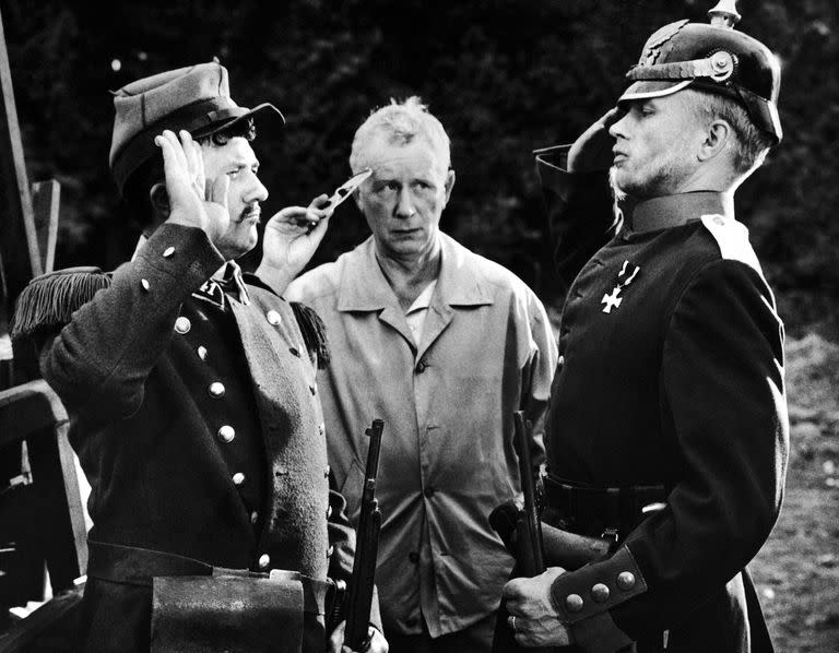 El director alemán Helmut Kaeutner, en el centro, muestra al actor alemán Hardy Krüger, a la derecha, y al actor francés Jean Richard cómo saludar durante el rodaje en Francia de Sin trompeta ni tambor, una comedia ambientada en la guerra franco-prusiana de 1870