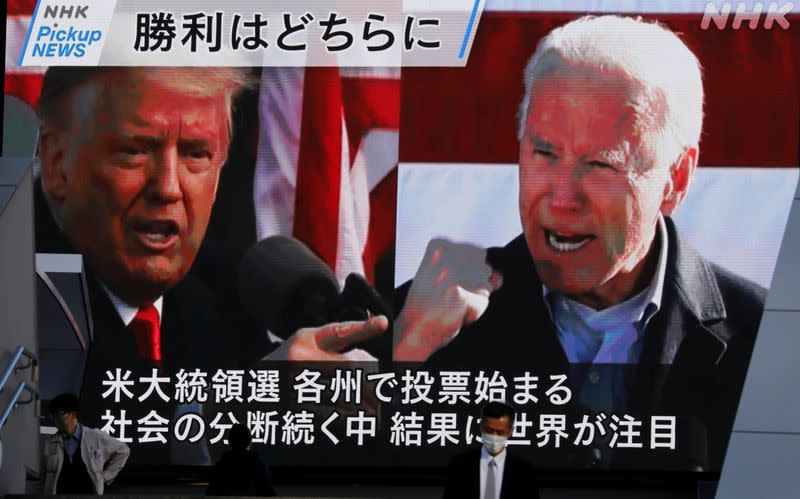 Pedestrians walk past a large screen showing news on 2020 U.S. presidential election in Tokyo