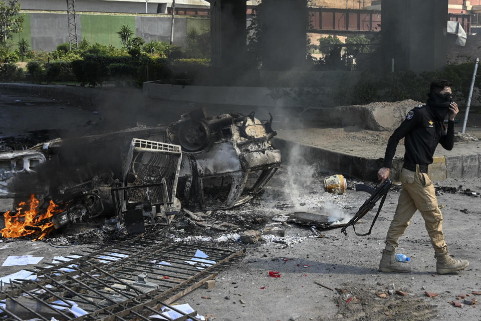 A policeman holding a machine gun walks past a burning car during a protest by Pakistan Tehreek-e-Insaf (PTI) party activists and supporters of former Pakistan's Prime Minister Imran over the arrest of their leader, in Peshawar, May 10, 2023. / Credit: ABDUL MAJEED/AFP/Getty