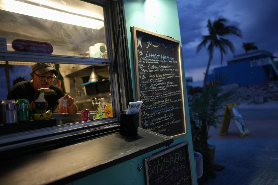 A man works inside the Yo Samara's food truck in the Times Square area of Fort Myers Beach, Fla., Wednesday, May 10, 2023. Though many businesses remain closed and some do not plan to return, food trucks and campers now dot the Times Square area and other points along the beach, as restaurants and bars find ways to reopen without their former infrastructure. (AP Photo/Rebecca Blackwell)