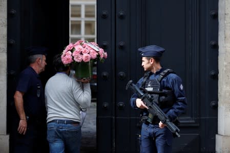 A man carries flowers as French police stand in front of the building where former French President Jacques Chirac was living in Paris