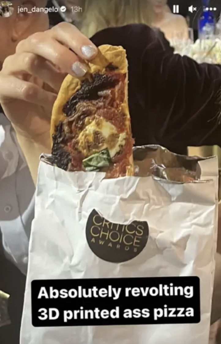 Person holding a slice of pizza with a Critics' Choice Award bag nearby. Text on image criticizes the pizza