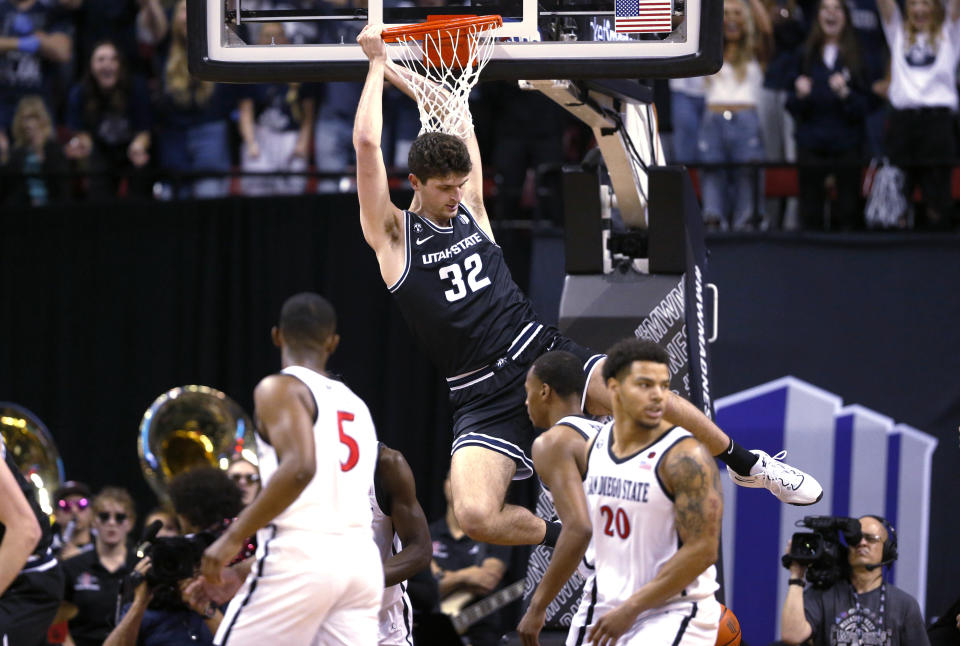 Utah State center Trevin Dorius (32) hangs from the rim after dunking against San Diego State during the first half of an NCAA college basketball game for the men's Mountain West Tournament championship Saturday, March 11, 2023, in Las Vegas. In the foreground are San Diego State guards Lamont Butler (5) and Matt Bradley (20). (AP Photo/Steve Marcus)
