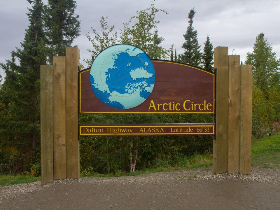 A sign next to pine trees for the Arctic Circle.