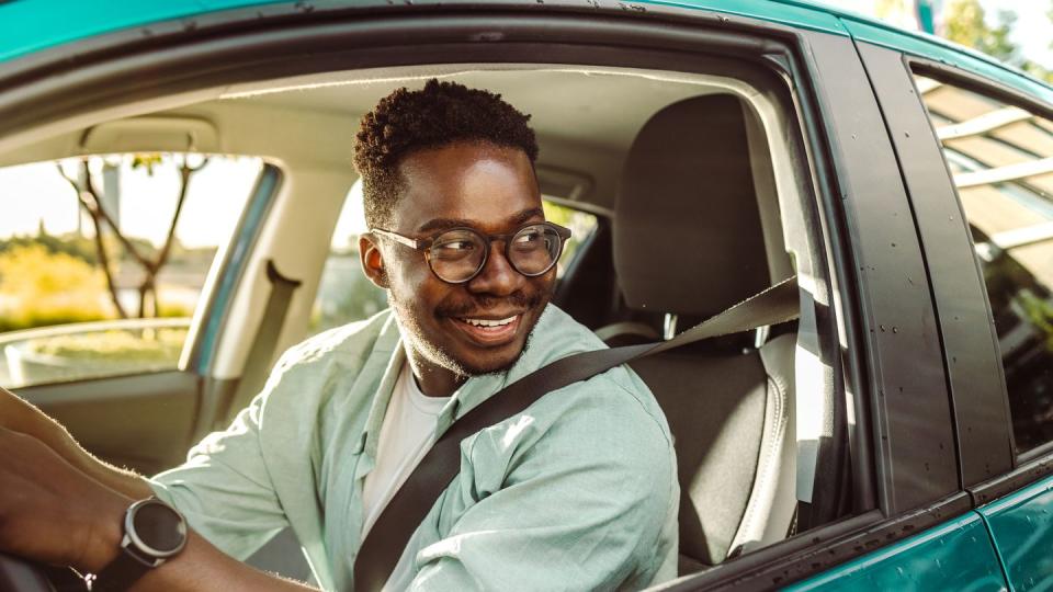 happy african american male driver driving a car and looking through the car window