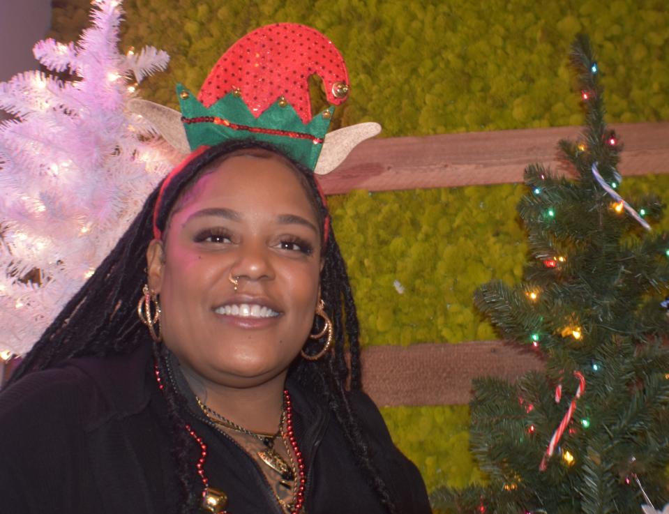 Tierra Stewart, a budtender at Nova Farms in Woodbury, stands against a backdrop of holiday trees and marijuana buds (all artificial).