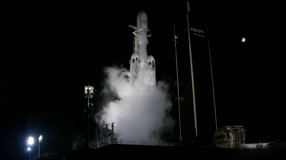 a white spacex falcon heavy rocket sits on the launch pad at night