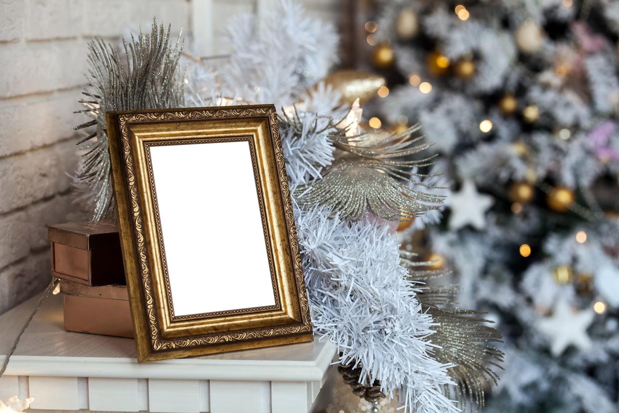 Gold ornate picture frame on a mantle with a decorated Christmas tree in the background