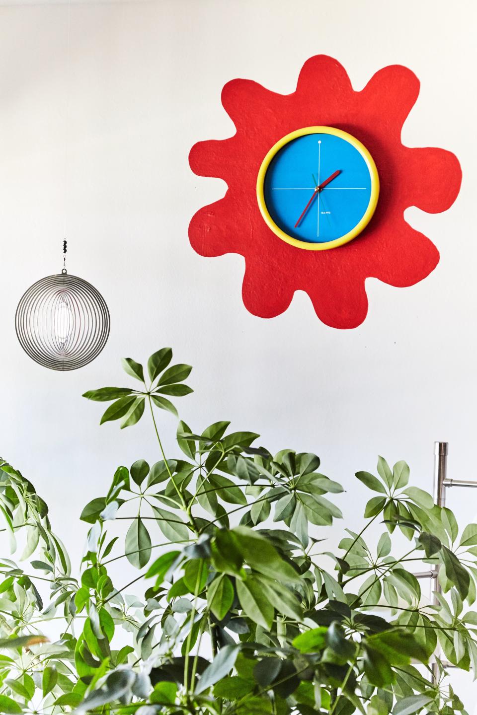 Leah created her version of an indoor garden using a laser-cut metal hanging—a gift from her sister, who lives in South Africa—hung above a tree next to an unconventional sun. “Love that clock. It's from the ’80s, obviously, and then I painted that red squiggle around it. It's my favorite moment in my apartment probably.”