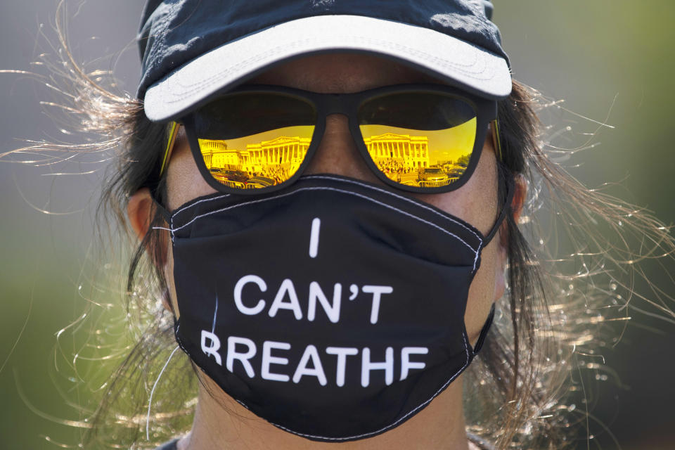 Debbie Ho of Washington, D.C. watches a news conference, reflected in her sunglasses, on the House East Front Steps on Capitol Hill in Washington, Thursday, June 25, 2020, as she wears a facemark that reads "I CAN'T BREATH" ahead of the House vote on the George Floyd Justice in Policing Act of 2020. (AP Photo/Carolyn Kaster)