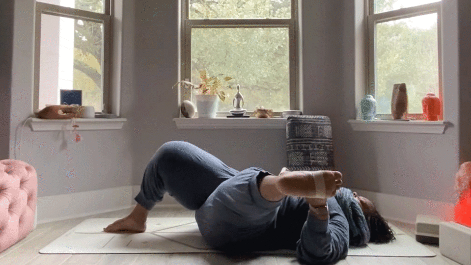 Woman stretching her hip and hamstring while lying on her back in her bedroom