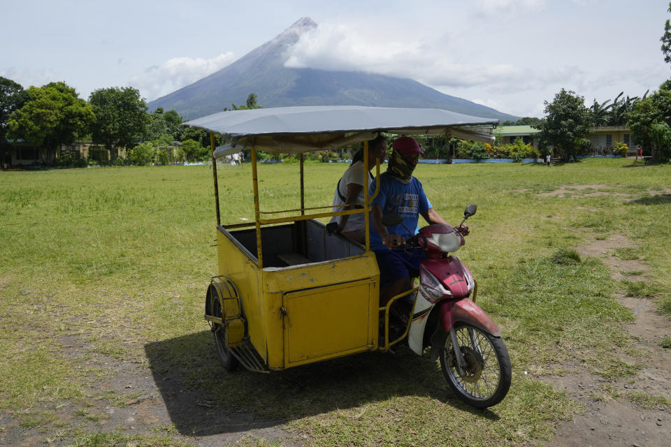 Mayon Volcano is seen as a tricycle passes by an evacuation center in Santo Domingo town, Albay province, northeastern Philippines, Tuesday, June 13, 2023. Truckloads of villagers on Tuesday fled from Philippine communities close to gently erupting Mayon volcano, traumatized by the sight of red-hot lava flowing down its crater and sporadic blasts of ash. (AP Photo/Aaron Favila)