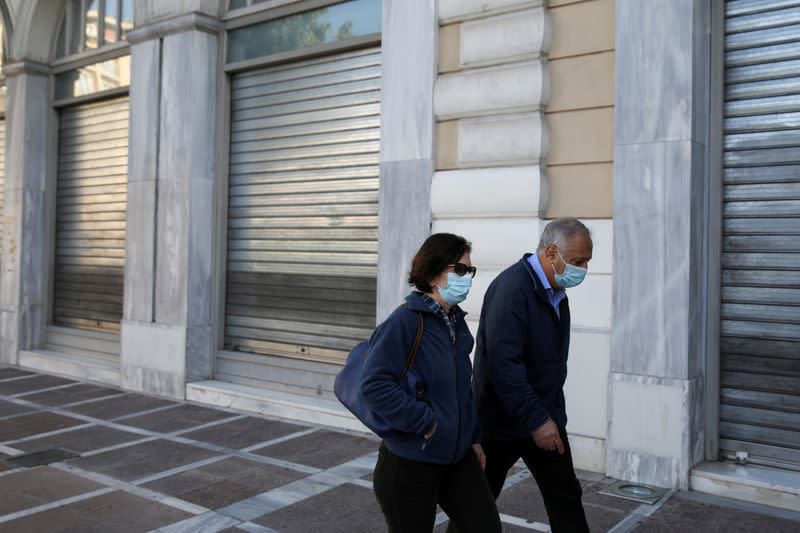 FILE PHOTO: People wearing protective face masks walk past a closed shop, amid lockdown restrictions due to the spread of the coronavirus disease (COVID-19) pandemic, in Athens