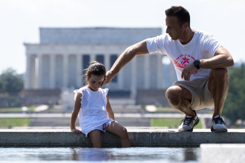 A man holds a hand to a young girl's face with a white-pillared building in the background