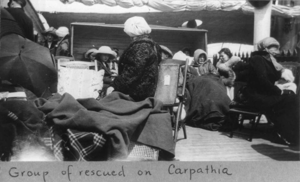 Wrapped in shawls and blankets survivors sit on the deck of the Carpathia.