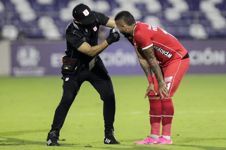 Un asistente ayuda a Duvan Vergara, delantero de América de Cali, afectado por los gases lacrimógenos que se lanzaron fuera del estadio Romelio Martinez de Barranquilla, pero cuyos efectos llegaron hasta el campo de juego