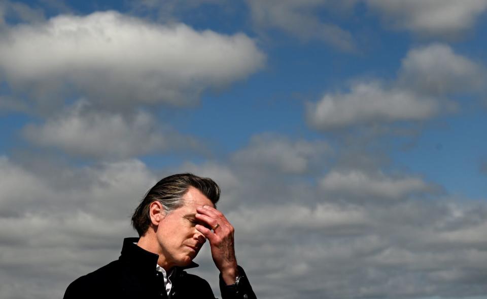 Gov. Gavin Newsom holds his head while speaking to reporters in Pajaro.