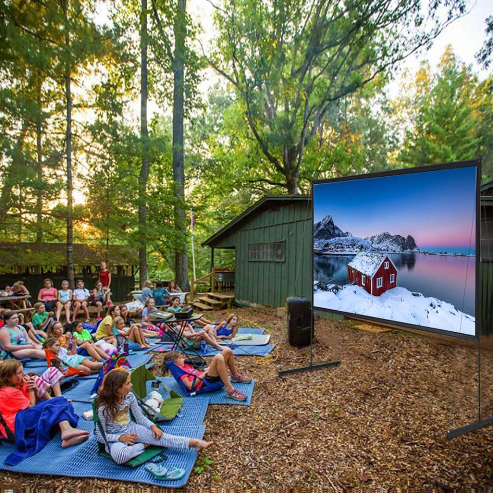 Outdoor movie night with people sitting on blankets and chairs, watching a large screen amidst trees