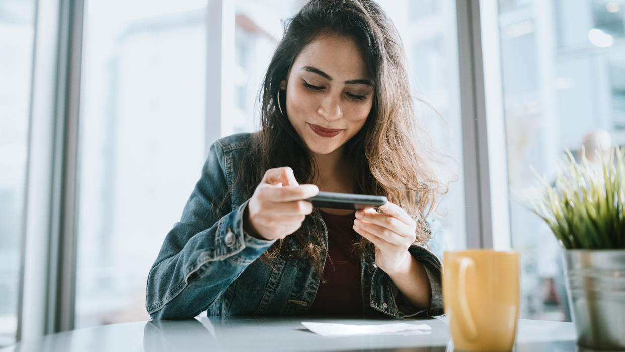 A smiling young Indian woman sends her paycheck to the bank via Remote Deposit Capture with her mobile phone.