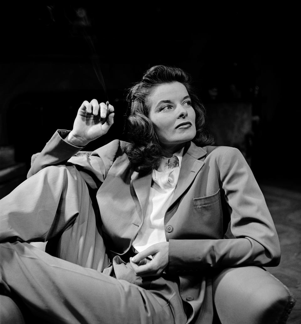 An undated portrait of actress Katharine Hepburn wearing a suit, with a cigarette in her hand.