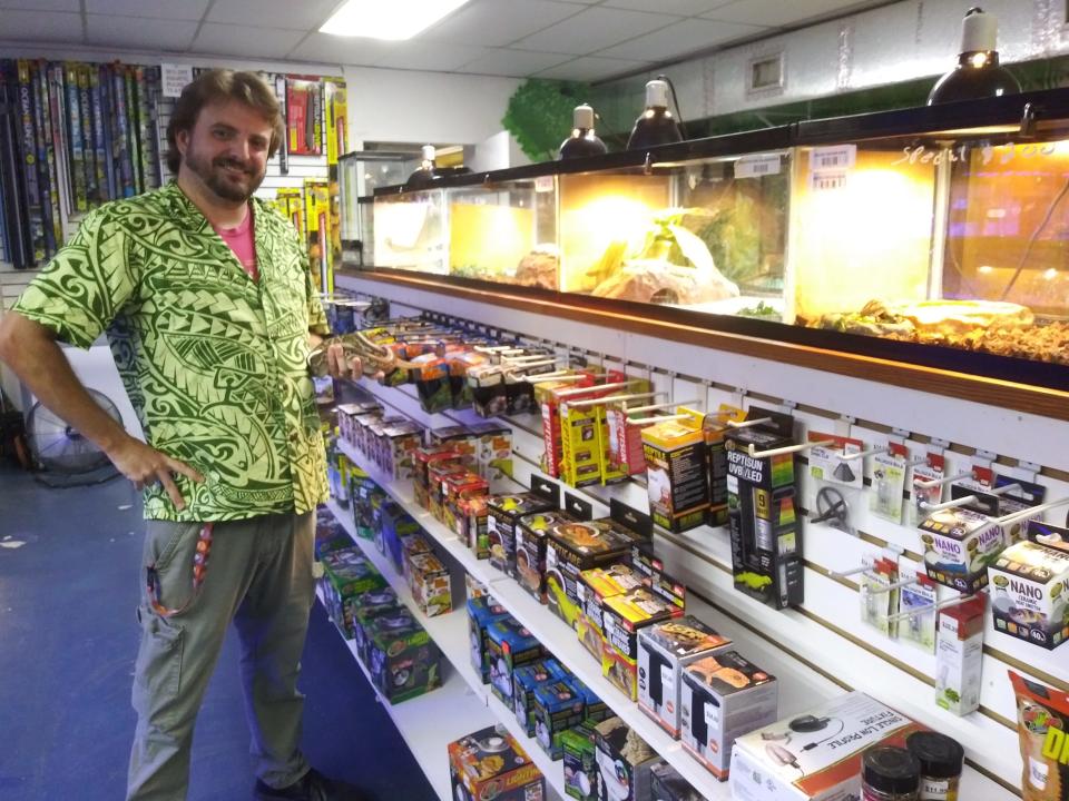 Curtis Elliott, a full-time volunteer at Snails and Tails reptile shop in Holly Hill, poses with a ball python among other reptiles offered at the store.