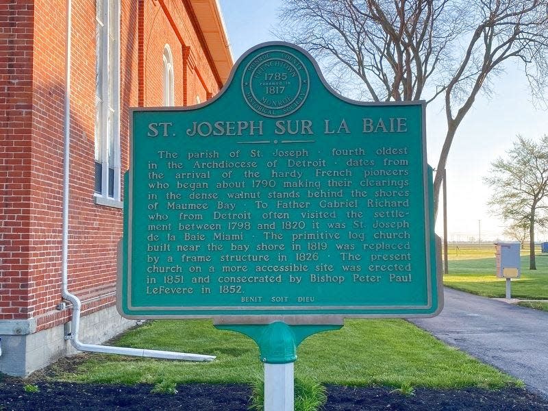 This is an image of the Michigan Historical Marker for the St. Joseph Catholic Church in Erie. The marker includes the French reference sur la baie (“on the bay”), related to the French Canadian Catholics that settled in the area. At the bottom of the marker is the phrase “Benit Soit Dieu" "Blessed is God."