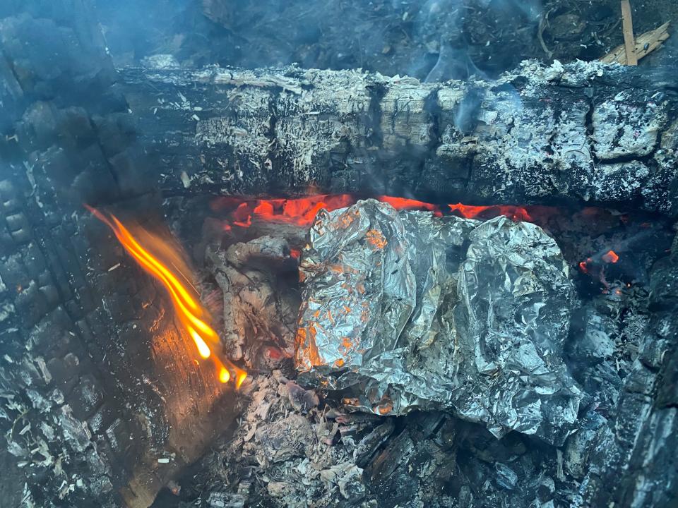 The tinfoil wrapped filets cooking on a bed of campfire embers.