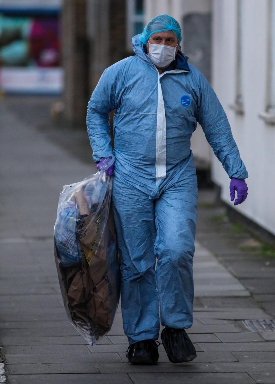 A forensic investigator carries evidence away from the scene (Alex Lentati)