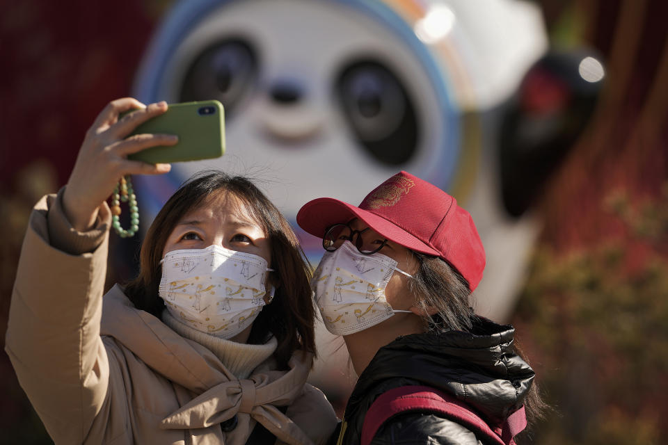 Residents wearing face masks to help protect from the coronavirus take a selfie with the Olympic mascot Bing Dwen Dwen decoration in Beijing, Tuesday, Feb. 8, 2022. China has ordered inhabitants of the southern city of Baise to stay home and suspended transportation links amid a surge in COVID-19 cases at least partly linked to the omicron variant. (AP Photo/Andy Wong)