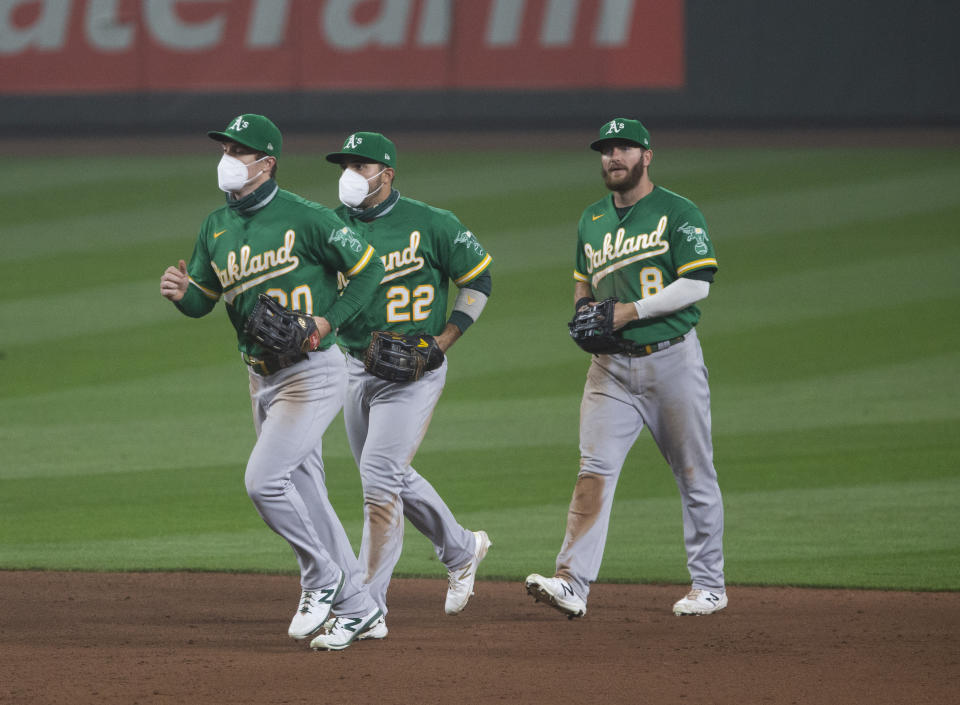 The Oakland A's outfield jogs in during a 2020 game, with Mark Canha and Ramon Laureano wearing masks. The 2021 season is likely to be played under the same sort of protocols. (Photo by Lindsey Wasson/Getty Images)