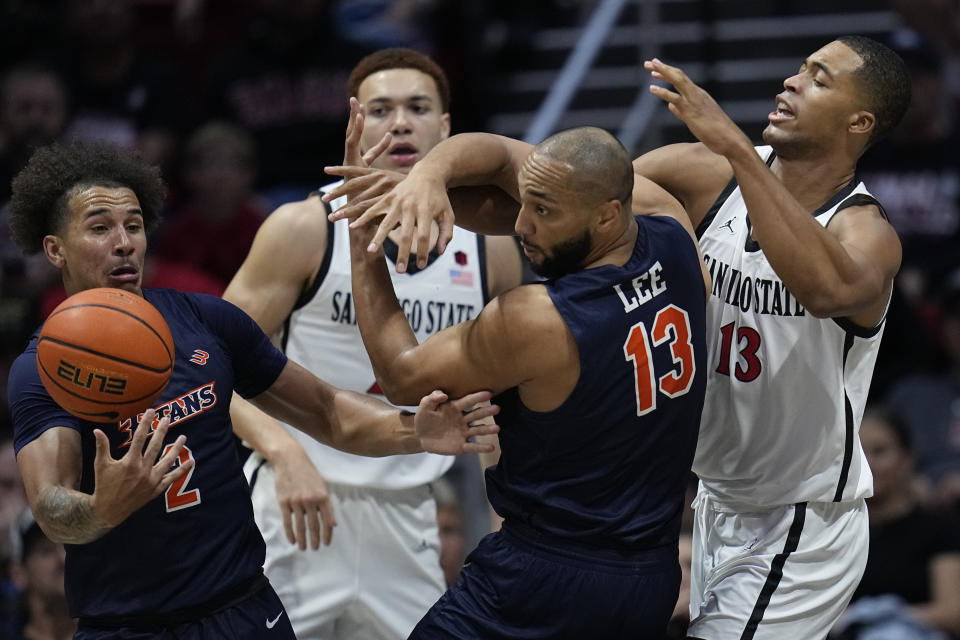 Cal State Fullerton guard Max Jones, left, and teammate forward Vincent Lee (13) battle for a loose ball with San Diego State forward Jaedon LeDee (13) as San Diego State forward Elijah Saunders looks on, behind, during the first half of an NCAA college basketball game, Monday, Nov. 6, 2023, in San Diego. (AP Photo/Gregory Bull)
