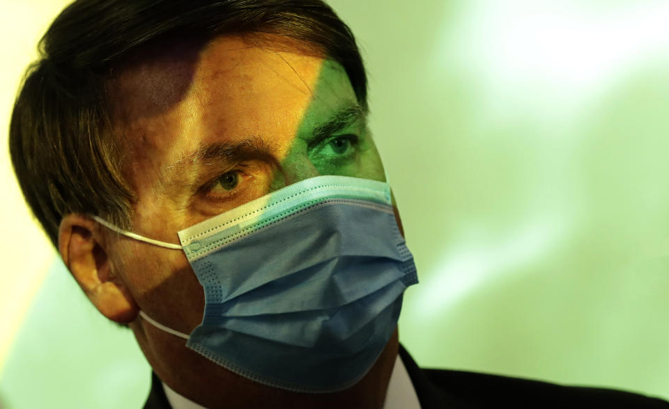 Brazil's President Jair Bolsonaro wears a mask amid the COVID-19 pandemic at the start of a ceremony where his nation's flag is projected over him in Brasilia, Brazil, Wednesday, Aug. 5, 2020. In May, facing urgent international demands for action after a string of massive wildfires in the Amazon, Brazilian President Jair Bolsonaro put the army in charge of protecting the rainforest. (AP Photo/Eraldo Peres)