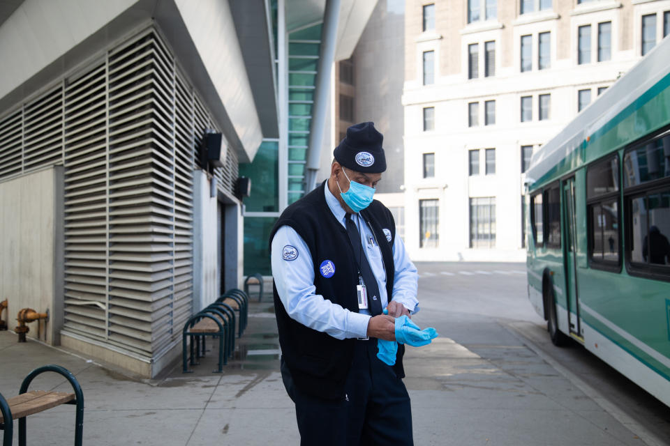 Image: A bus driver wearing a protective mask changes gloves at the Rosa Parks Transit station in Detroit (Emily Elconin / Bloomberg via Getty Images)