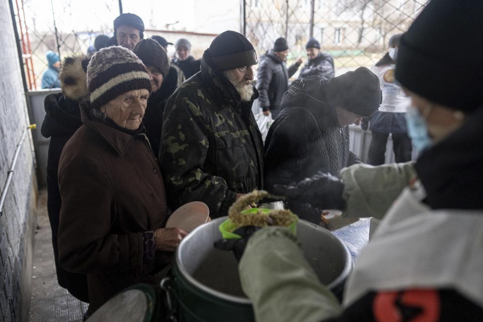 Local residents wait in line to receive a hot meal from volunteers of "World Central Kitchen", after living without electricity for more than four months in Kupiansk, Kharkiv region, Ukraine, Wednesday, Dec. 28, 2022. (AP Photo/Evgeniy Maloletka)
