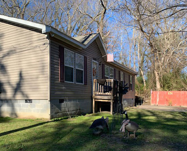 One-story house with cinder block foundation and American flag over door and what appear to be two statues of Canadian geese in front lawn.