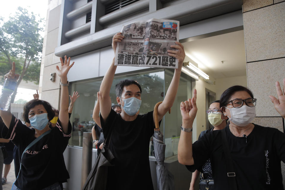 Protesters gesture with five fingers, signifying the "Five demands - not one less" and hold a copy of the Apple Daily newspaper outside a court during a protest in Hong Kong, Thursday, Aug. 27, 2020. Hong Kong police arrested 16 people, including two opposition lawmakers, on Wednesday on charges related to anti-government protests last year. (AP Photo/Kin Cheung)