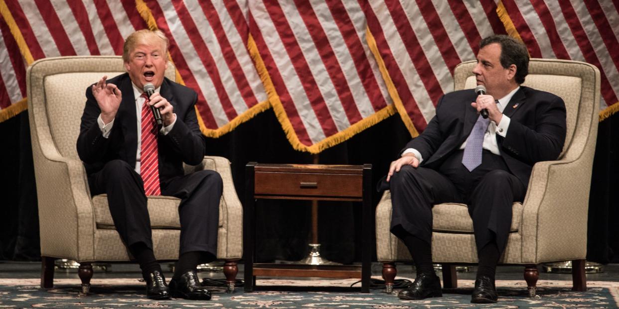 Donald Trump sitting on a stage and talking into a microphone adjacent to Chris Christie.