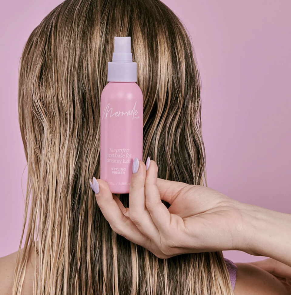 Woman holds bottle of Mermade Hair styling primer behind her head