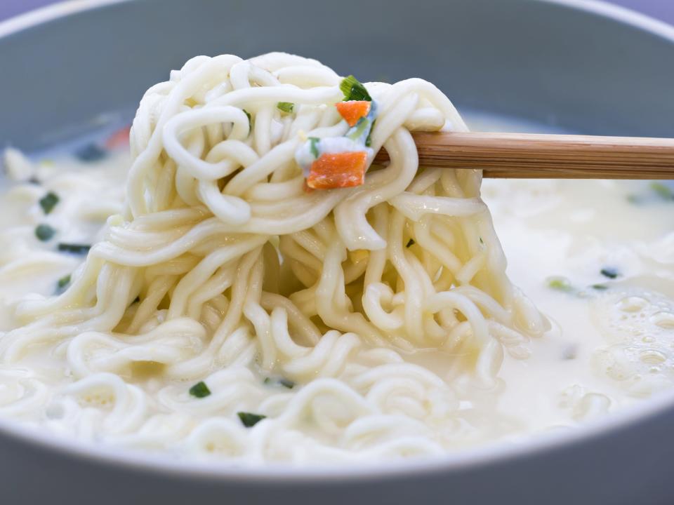 noodles being pulled out of a soup with chopsticks