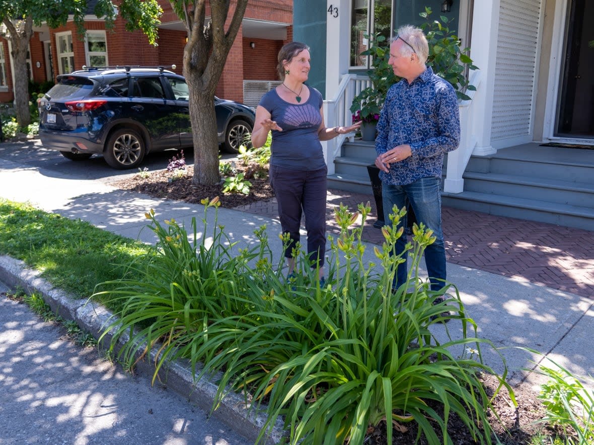 Raewyn Khosla, left, and Andrew Fyfe chat in front of Fyfe's home on Alexander Street in Ottawa's New Edinburgh neighbourhood last summer. Under proposed amendments to the city's right-of-way bylaw, Fyfe's verge garden would remain illegal because it's planted within one metre of the curb. (Francis Ferland/CBC - image credit)