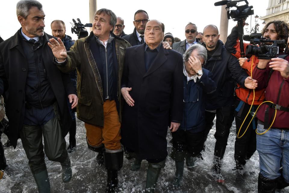 Former Italian Premier Silvio Berlusconi, center, flanked by Venice mayor Luigi Brugnaro, left, and MP Renato Brunetta, wades through water in St. Mark's Square in Venice, Italy, Thursday, Nov. 14, 2019. The worst flooding in Venice in more than 50 years prompted calls to better protect the historic city from rising sea levels as officials calculated hundreds of millions of euros in damage. (AP Photo/Luigi Costantini)