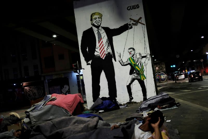 FILE PHOTO: Homeless people rest in front of graffiti depicting U.S. President Donald Trump and Brazilian president Jair Bolsonaro underneath Minhocao bridge in Sao Paulo