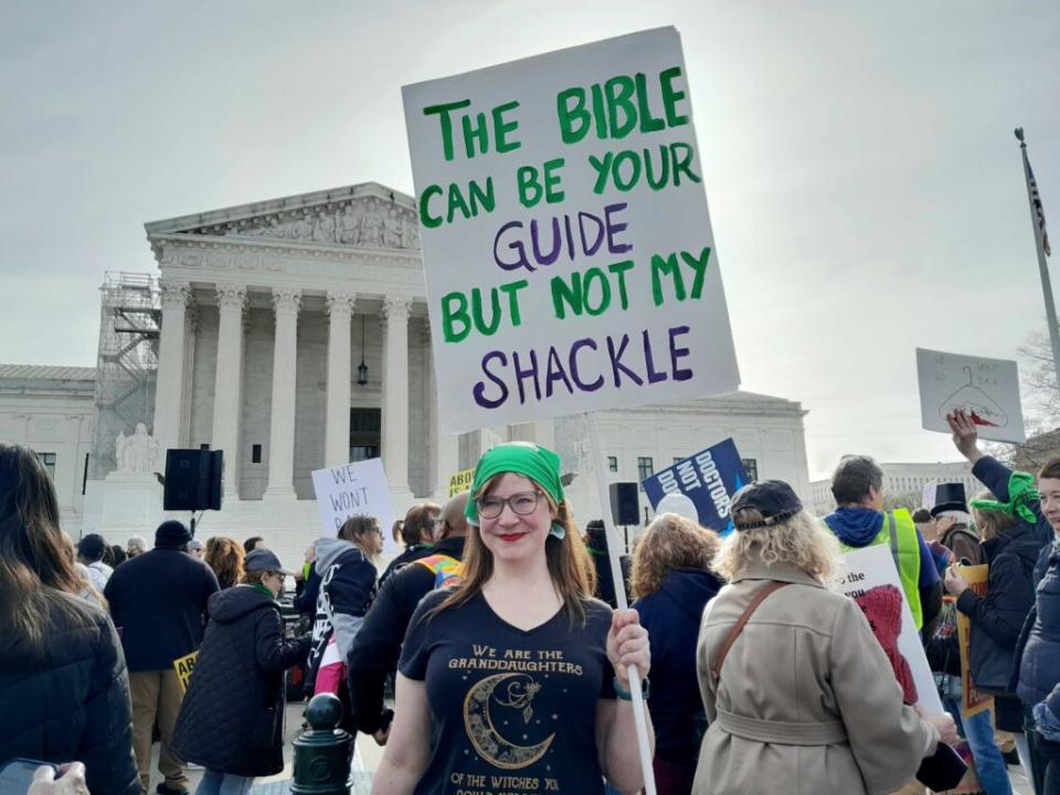 A woman holding a sign saying "The Bible Can Be Your Guide But Not My Shackle."