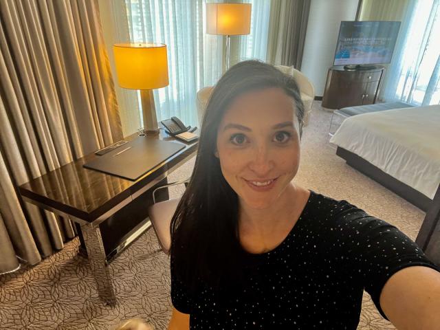 A woman taking a selfie in front of a hotel bedroom.
