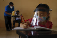 Wearing a mask and a face shield to curb the spread of the new coronavirus, 10-year-old Jade Chan Puc writes in her workbook during the first day of class at the Valentín Gomez Farias Indigenous Primary School in Montebello, Hecelchakan, Campeche state, Monday, April 19, 2021. Campeche is the first state to transition back to the classroom after a year of remote learning due to the pandemic. (AP Photo/Martin Zetina)