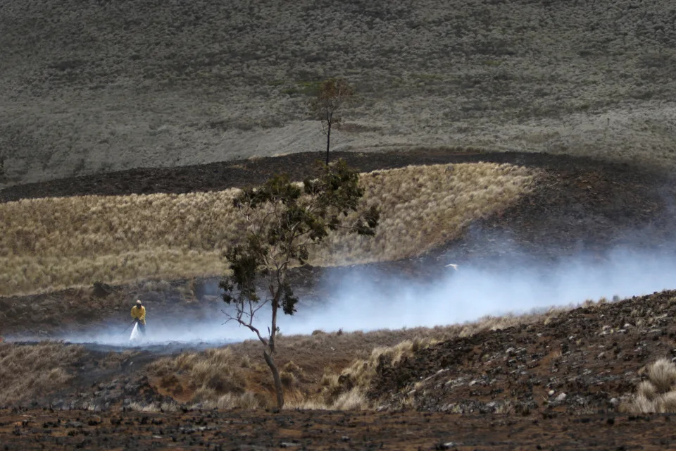 A Big Island firefighter hoses a blaze as a curtain of smoke rises.