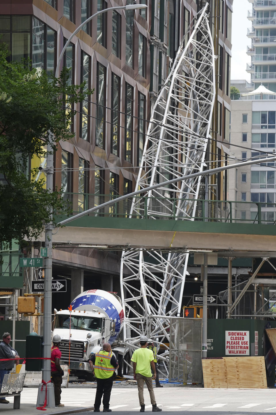 Part of the extension arm from a hi-rise construction crane lies crashed against a cement truck, Thursday July 27, 2023, in New York. The crane caught fire yesterday, losing the long arm which smashed into a nearby building as it plummeted to the street. (AP Photo/Bebeto Matthews)